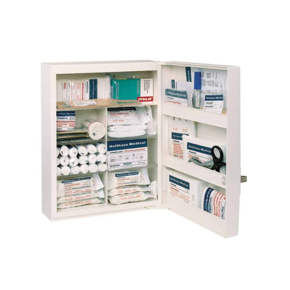 L'armoire à pharmacie FAMULUS de Holthaus Medical GmbH & Co. KG, non équipée, est une armoire de premiers secours ouverte et spacieuse, dotée de plusieurs étagères pouvant accueillir divers articles médicaux tels que des bandages, des rouleaux de gaze, un masque de RCP, des lingettes antiseptiques et des pansements adhésifs. Son agencement clair garantit une identification et un accès faciles en cas d'urgence. Un symbole de secours est clairement apposé sur la porte pour permettre une identification rapide.