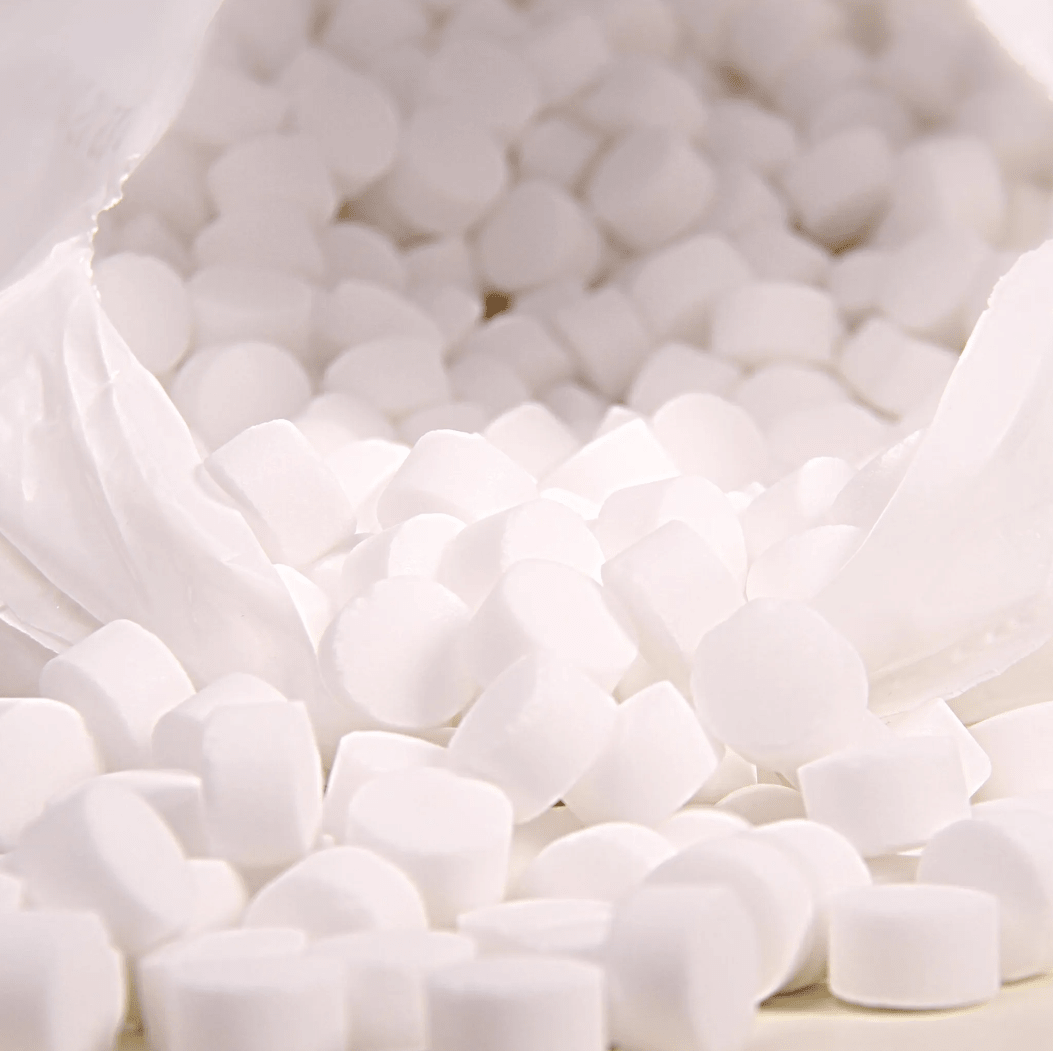 Un gros plan montre un sac en plastique blanc portant l'inscription « K+S Minerals and Agriculture GmbH », contenant des pastilles de sel d'évaporation Regenit conformes à la norme EN 973, type | sac (25 kg), qui tombent sur une surface. Ces petites pastilles rondes ont une forme et une taille uniformes et sont idéales pour une utilisation dans les adoucisseurs d'eau.