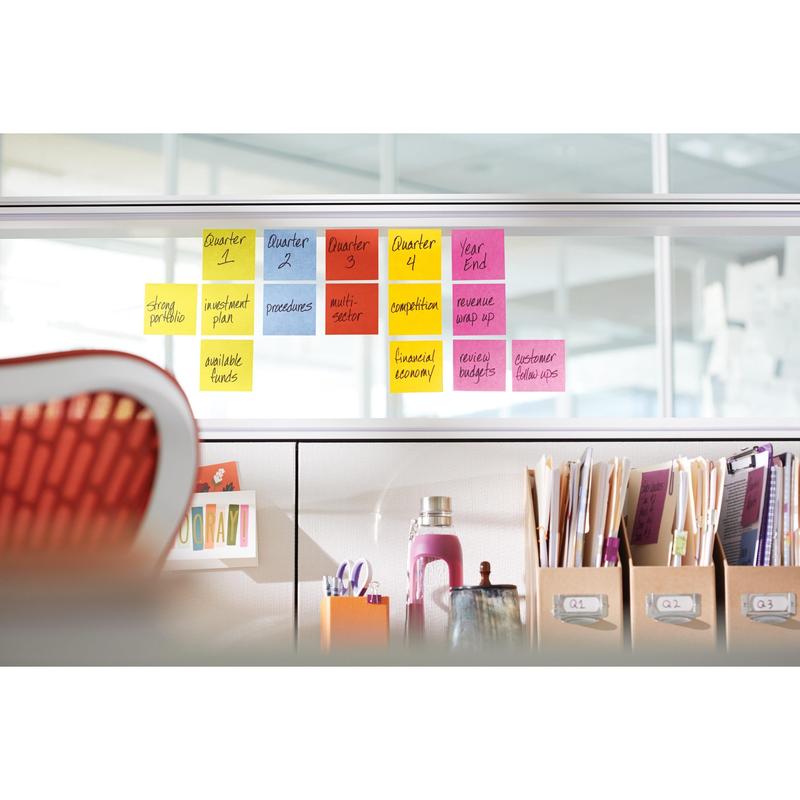 Une rangée de Post-it® Notes 3M, Jaune, 76x76 mm (90 feuilles/bloc, 6 blocs/paquet) est disposée sur un séparateur en verre ; en dessous se trouvent sur un bureau des classeurs, des livres, une bouteille d'eau et d'autres fournitures.