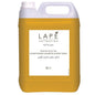 Un bidon transparent de 5 litres avec un couvercle blanc, rempli de liquide jaune. L'étiquette indique "LAPĒ Collection Oriental Lemon Tea Shampoo & Body Wash, Gel douche & Shampooing au parfum oriental" de Diversey Deutschland GmbH & Co. OHG.