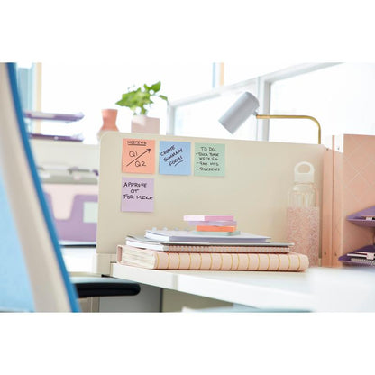 Un bureau moderne avec des carnets, une bouteille d'eau, un Post-it® Super Sticky Notes (76 x 127 mm, 90 feuilles, 100% PEFC) de 3M Deutschland GmbH sur une cloison, une lampe et des classeurs en arrière-plan. Certaines notes montrent des rappels et des tâches.