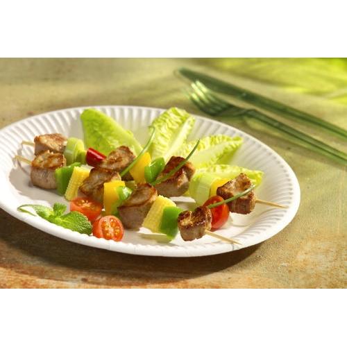 Une PAPSTAR assiette en carton ronde Ø 26 cm, extra forte, blanche "pure" de PAPSTAR GmbH tient deux brochettes avec de la viande grillée, des tomates cerises, des tranches de concombre et du poivron jaune sur de la salade et de la menthe; en arrière-plan, des couverts en plastique vert.
