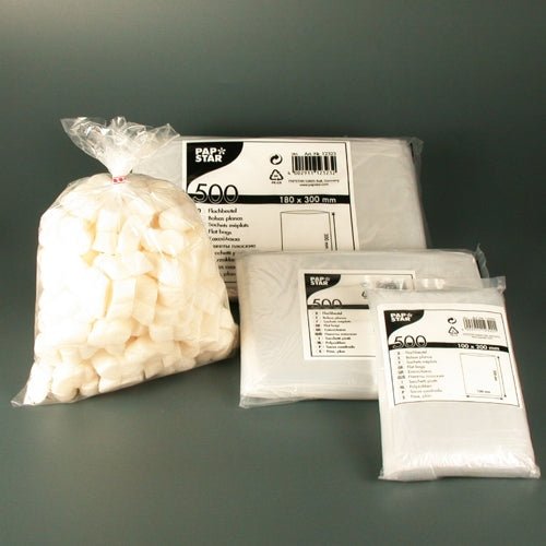 Un ensemble de produits de la société PAPSTAR GmbH, composé d'un sac de sucre en morceaux blanc et de trois paquets de PAPSTAR 500 sachets plats LDPE transparents de différentes tailles, présenté sur un fond gris simple comme solutions d'emballage transparentes.
