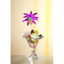 Un bol à dessert en verre avec de la glace lumineuse, des fruits et des mûres est élégamment décoré avec un pique à cocktail "Feuilles de palmier" de 19,5 cm (assorti par couleur) de la PAPSTAR GmbH, provenant de l'ensemble de 50 pièces en plateau en carton, devant un fond jaune pâle.