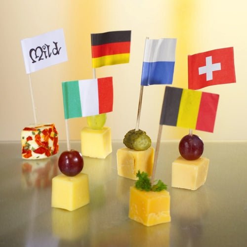 Cinq cubes de fromage, chacun avec une garniture unique et un drapeau différent, sont disposés sur un PAPSTAR 100 Deko-Picker de haute qualité et robuste de la société PAPSTAR, sur une surface réfléchissante - idéal pour des présentations élégantes lors de tout événement international.