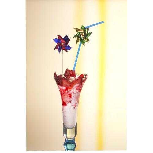 Un grand verre avec une boisson glacée rose et blanche, garnie de morceaux de fraise et de deux PAPSTAR 100 piques de décoration de PAPSTAR GmbH ainsi qu'une paille bleue, sur un fond clair avec une bande jaune.
