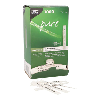 Une boîte distributrice partiellement ouverte de cure-dents "pure" PAPSTAR (1000 pièces) de la société PAPSTAR GmbH montre des cure-dents en bois ronds de 6,5 cm, emballés individuellement ; devant, plusieurs cure-dents emballés en blanc sont disposés.