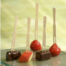 Sur cinq brochettes de finger food "pure" (8,5 cm) de la PAPSTAR GmbH, deux fraises, deux cubes de chocolat et une tranche de pomme sont embrochés, présentés verticalement sur un verre devant un fond vert clair.