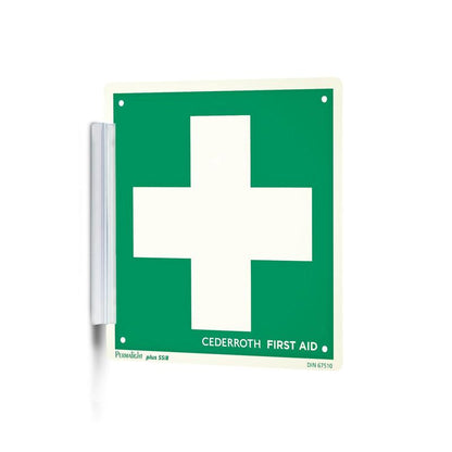 Un "Clip signer | Paquet (1 pièce)" vert-blanc de Orkla Wound Care AB avec une grande croix blanche et l'inscription "Cederroth First Aid" est fixé au mur comme un tampon de signature avec un support métallique et est ainsi bien visible sur le lieu de travail.