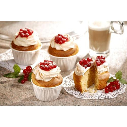 Dans les moules à muffins PAPSTAR GmbH Ø 5 cm, 3,5 cm de haut, blanc (20 pièces) se trouvent quatre cupcakes avec glaçage blanc et baies rouges sur un plan de travail. L'un est coupé. En arrière-plan, on peut voir une branche de menthe et un verre de latte.