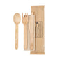 Le set de couverts Duni GmbH 4/1 en bois ciré naturel contient une fourchette, un couteau, une cuillère et une serviette marron (160/165/160), emballé hygiéniquement par 250 pièces - respectueux de l'environnement sur fond blanc à côté d'un sac en papier illustré.