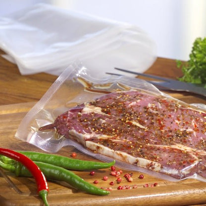 Un sachet à souder Starpak 100, PA/PE transparent, rempli de viande crue marinée est posé sur une planche à découper en bois. Des piments colorés et des légumes verts soulignent la fraîcheur obtenue avec une machine à vide à cloche de Starpak.