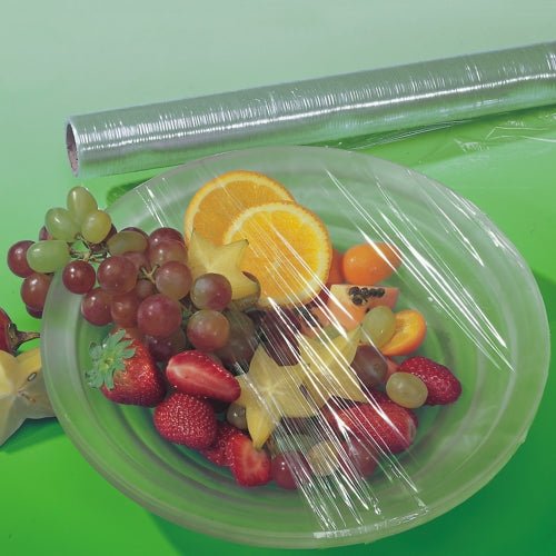 Un bol avec divers fruits est recouvert de film alimentaire perforé Starpak, tandis qu'un rouleau inutilisé de Starpak repose derrière sur une surface verte - parfait pour garder les aliments frais.