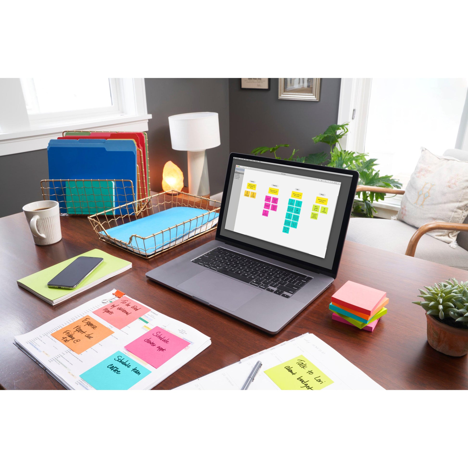Ein aufgeräumter Bürotisch mit einem Laptop, auf dem ein digitaler Organizer, farbcodierte Ordner, ein Telefon, eine Lampe, eine Zimmerpflanze, Notizzettel und eine Packung 3M Deutschland GmbH Post-it® Notes Poptimistic Collection (38mm x 51mm) zu sehen sind, beleuchtet vom Sonnenlicht des Fensters.
