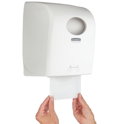 Une personne tire une serviette en papier d'un distributeur de serviettes en rouleau Aquarius™ - Blanc de Kimberly-Clark GmbH avec ouverture circulaire et graphique instructif - idéal pour les espaces publics.