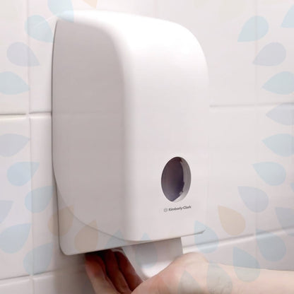 Une cartouche de lotion lavante douce Kleenex® de Kimberly-Clark GmbH (transparente, 1 L) est illustrée sur un mur carrelé blanc, avec une main tirant une serviette du bas et une petite fenêtre ronde à l'avant. Disponible en paquets de 6 cartouches.