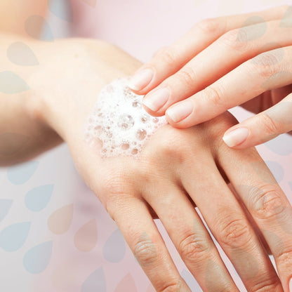 Une personne utilise la lotion lavante douce Kleenex® (cartouche de 1L) de Kimberly-Clark GmbH pour un nettoyage doux des mains et applique le savon moussant sur le dos des mains devant un fond clair avec un motif subtil de gouttes d'eau.