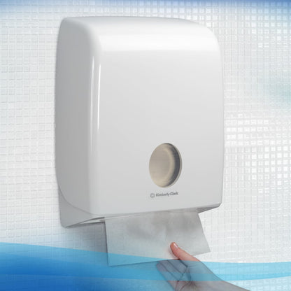 Une main retire une serviette pliée absorbante Scott® CONTROL™ de Kimberly-Clark GmbH d'un distributeur mural blanc pour le séchage hygiénique des mains, monté sur un mur carrelé.