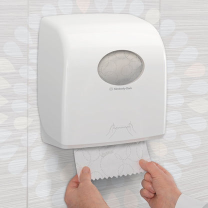 Quelqu'un tire une serviette Kleenex® Ultra™ Slimroll™ d'un distributeur blanc monté au mur avec une fenêtre de visualisation et des symboles dans des toilettes carrelées. Produit : carton de 6 rouleaux de Kimberly-Clark GmbH.