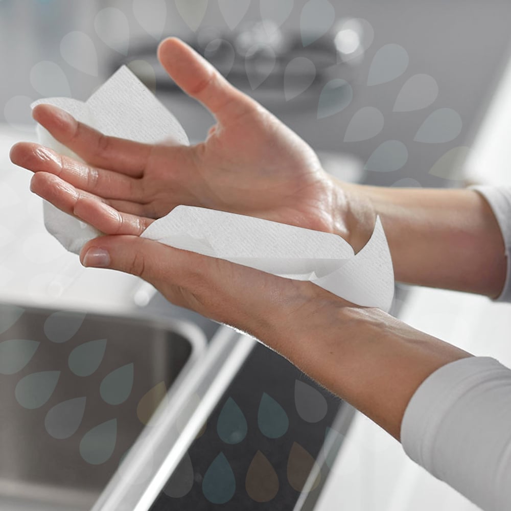 Une personne sèche ses mains au-dessus d'un évier avec des mouchoirs pliants Kleenex® - Blanc/Grand (15 paquets x 124 feuilles | carton) de Kimberly-Clark GmbH, avec les deux mains et une partie de l'évier visibles en arrière-plan.