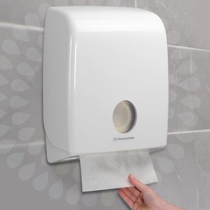 Une main tire une serviette Kleenex® Ultra™ d'un distributeur mural blanc de Kimberly-Clark GmbH, installé sur un mur carrelé (Interfold/Blanc/Grand - 30 clips x 94 feuilles | Carton, 30 paquets).