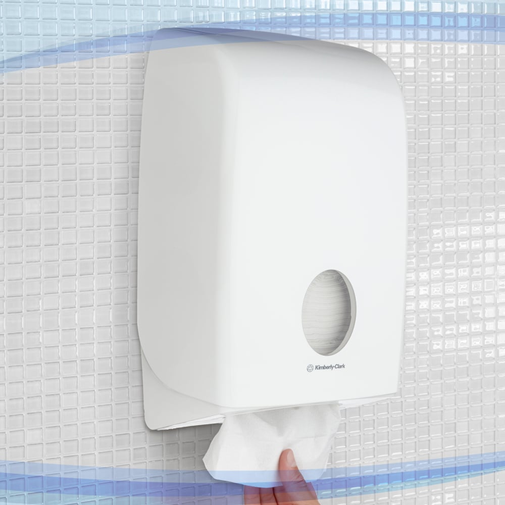 Une main tire une serviette en papier du distributeur blanc Aquarius™ pour serviettes pliées de Kimberly-Clark GmbH, monté sur une tuile au mur. Le distributeur a une fenêtre pour une distribution hygiénique et facile des serviettes.