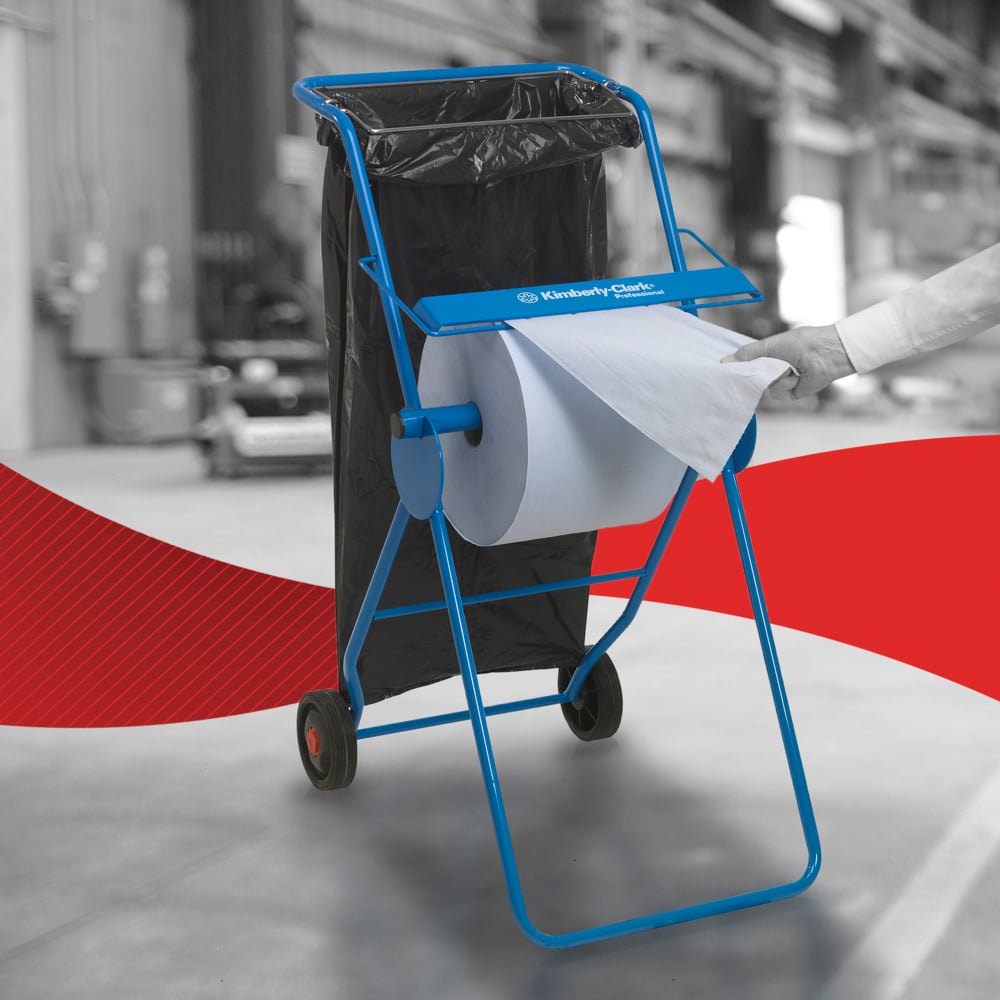 Une personne tire un papier essuie-tout WypAll® L10 pour surfaces - grand rouleau (38,00 x 23,50 cm) de Kimberly-Clark GmbH d'un support métallique bleu avec roulettes et un sac poubelle noir attaché, indiquant un nettoyage efficace des surfaces dans des environnements industriels.