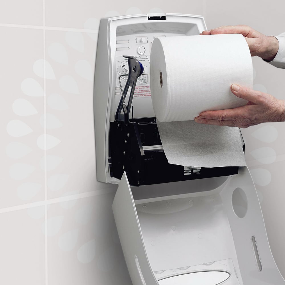 Une personne place un rouleau de serviettes Kleenex® Ultra™ de la société Kimberly-Clark GmbH dans un distributeur mural blanc ouvert, installé dans des toilettes, afin de garantir un séchage hygiénique des mains. Des instructions sont imprimées sur le couvercle du distributeur.