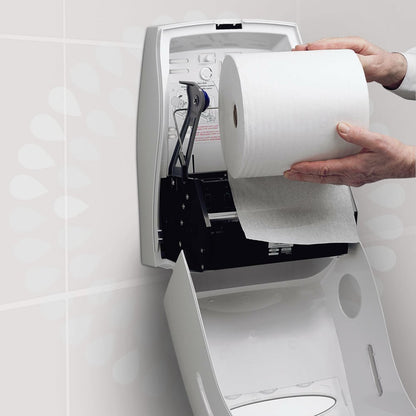 Une personne place un rouleau de serviettes Kleenex® Ultra™ de la société Kimberly-Clark GmbH dans un distributeur mural blanc ouvert, installé dans des toilettes, afin de garantir un séchage hygiénique des mains. Des instructions sont imprimées sur le couvercle du distributeur.