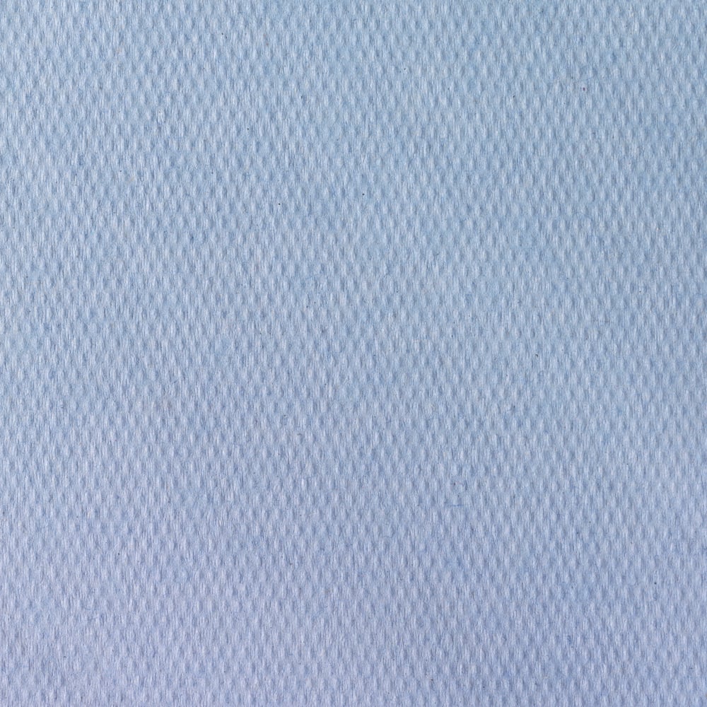 Nahaufnahme von Scott® Ärzterollen der Kimberly-Clark GmbH (38,00 cm x 51,00 cm), einem hellblauen, strukturierten Stoff mit dezentem Rautenmuster, der häufig für Untersuchungsliegen in medizinischen Einrichtungen verwendet wird. Die glatte Oberfläche füllt den Rahmen aus.