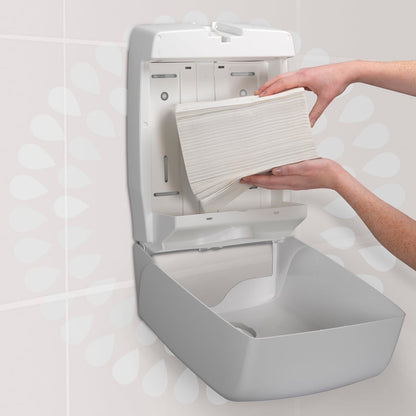 Une personne charge une pile de serviettes à main Kleenex® Ultra™ MultiFold de Kimberly-Clark GmbH (blanc, petit, 18 paquets x 150 feuilles) dans un distributeur mural de serviettes en papier dans une toilette.