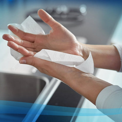 Une personne se sèche les mains avec un essuie-mains en rouleau Scott® Essential™ - E-roll Slimroll™ (Blanc, 1 épaisseur, 6x180m) de Kimberly-Clark GmbH au-dessus d'un évier de cuisine - idéal pour la maison ou les salles de bain.