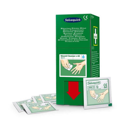 Une boîte verte de Salvequick savett nettoyant pour plaies (0,9% naci, stérile) 40 pièces de Orkla Wound Care AB est debout avec des sachets individuels devant; les deux montrent une main nettoyée avec une lingette.