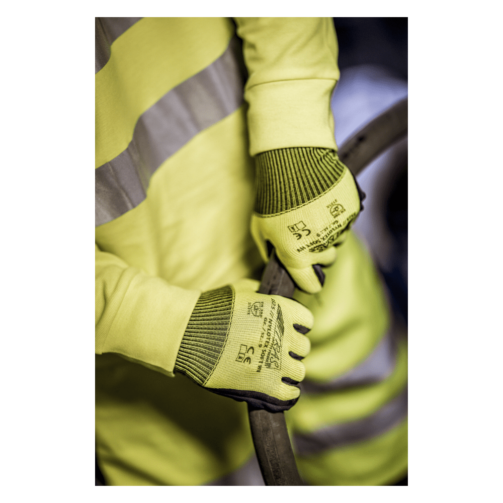 Une personne portant un gilet de sécurité jaune et des gants en nylon NITRAS NYLOTEX SOFT HV de AS Arbeitsschutz GmbH, jaune néon, partiellement enduits - avec texte noir et symboles de sécurité - tient un câble ou un tuyau épais et sombre.
