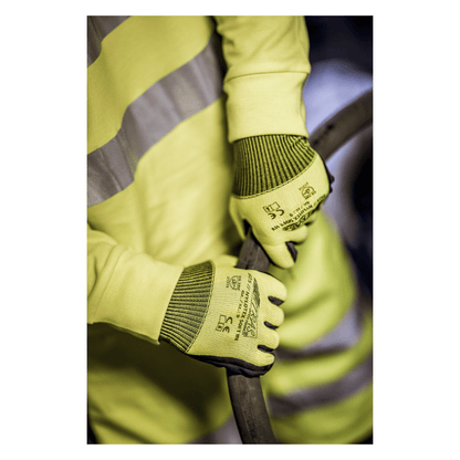 Une personne portant un gilet de sécurité jaune et des gants en nylon NITRAS NYLOTEX SOFT HV de AS Arbeitsschutz GmbH, jaune néon, partiellement enduits - avec texte noir et symboles de sécurité - tient un câble ou un tuyau épais et sombre.