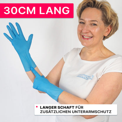Une personne en chemise blanche et gants en nitrile bleus de la société ARNOWA GmbH sourit et pointe vers la manchette de 30 cm. Sur une bannière rose est écrit "30CM LONG" et indique que les gants ARNOMED NITRIL BLUE XTRA LONG offrent une protection supplémentaire pour l'avant-bras.