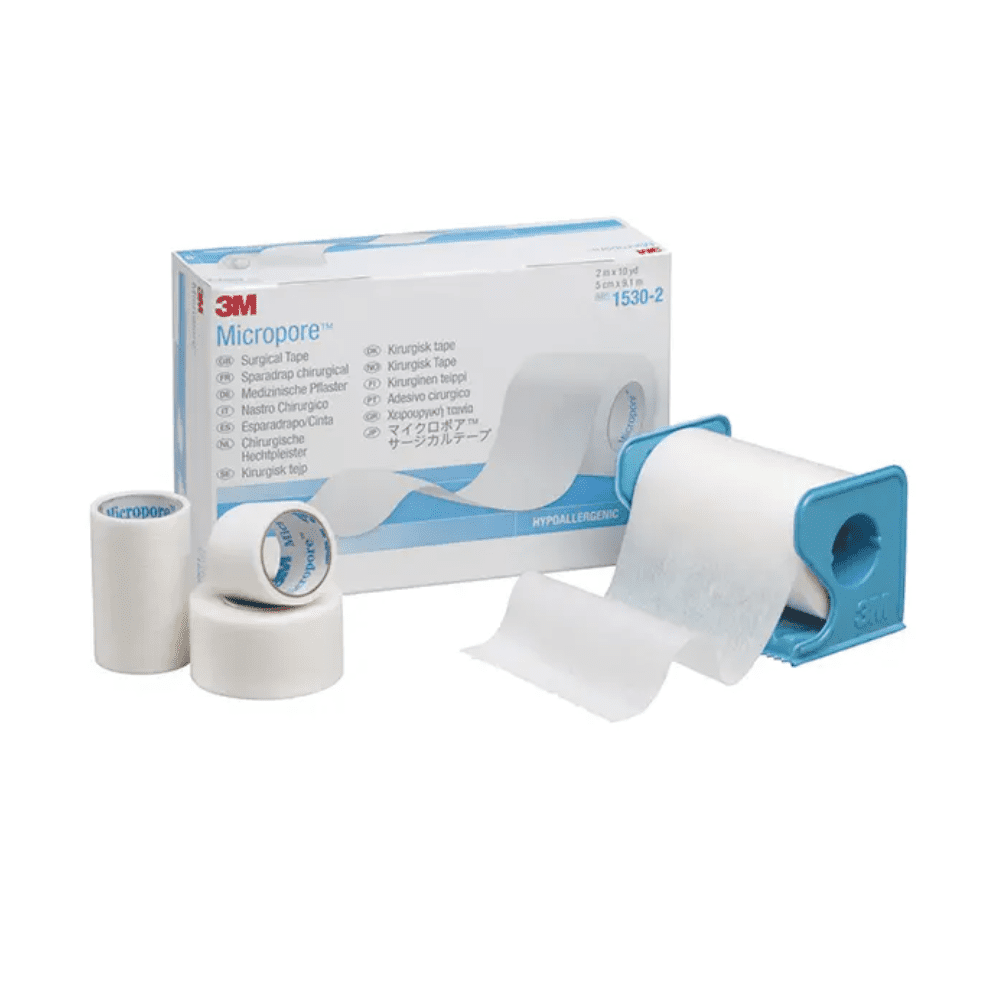 L'image montre un pansement Micropore 3M-Medica de 3M Healthcare Germany GmbH, couleur chair – 12 pièces | Boîte (12 pièces) avec des pansements de différentes tailles devant. Un rouleau de pansement se trouve dans un distributeur bleu, tandis que deux autres rouleaux de pansement et un plus petit rouleau se tiennent debout à côté de la boîte. Le pansement hypoallergénique est blanc.