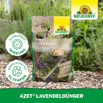 Un sac de Neudorff Shop Azet LavendelDünger est posé sur un chemin de jardin en gravier à côté de lavande avec des fleurs bleu-violet. Sur l'emballage, il est écrit "respectueux de l'environnement" en allemand.