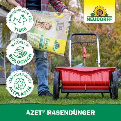 Une personne remplit un épandeur rouge avec Neudorff Shop Azet Engrais Gazon 2,5-5 kg pour favoriser des pelouses denses. Trois symboles indiquent qu'il est respectueux des animaux, biologiquement naturel et en plastique recyclé. Le logo Neudorff est visible.