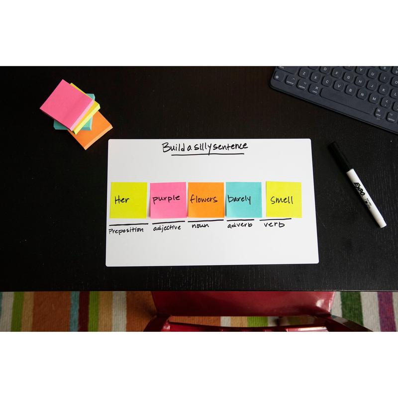 Sur un bureau noir se trouve un tableau blanc avec l'inscription "Construire une phrase amusante". Les cubes de notes Post-it® Ultra-Couleurs de 3M Deutschland GmbH, 76x76 mm, montrent les catégories de mots. Également sur le bureau : un marqueur effaçable à sec, un bloc-notes et un clavier.