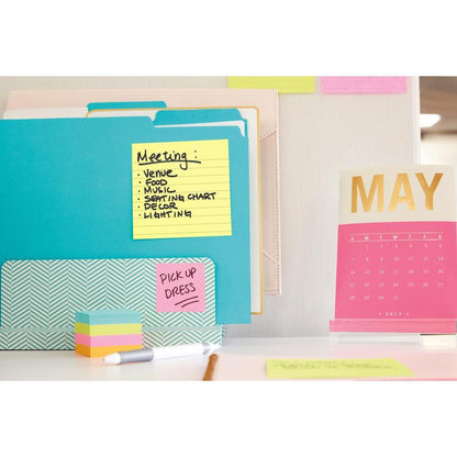 Un espace de travail avec des Post-it® Notes grand format, Jaune (101 mm x 152 mm) de 3M Deutschland GmbH, des classeurs, un calendrier de bureau rose-doré pour mai 2017 ainsi que des notes adhésives et des papiers colorés. Une feuille liste les sujets de "Meeting", sur une autre est écrit "PICK UP DRESS".