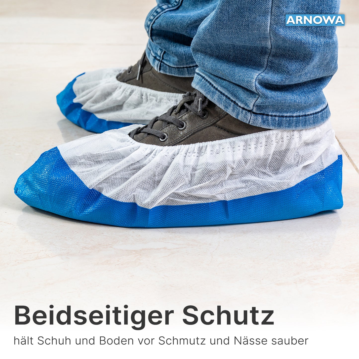 Une personne porte des couvre-chaussures ARNOMED CPE/PP de ARNOWA GmbH, imperméables et en bleu-blanc, sur des chaussures grises sur des carreaux clairs; le texte et la marque sont visibles.