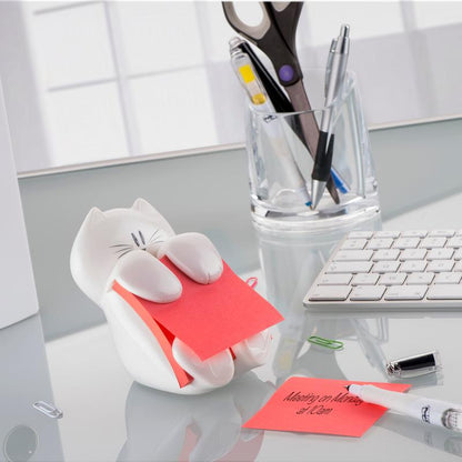Sur une table en verre se trouve le distributeur de notes Z Post-it® de 3M, chat, blanc avec une note Z Super Sticky rose Post-it® (76x76mm) de 3M Allemagne. À proximité, il y a un clavier, des stylos dans un gobelet en verre, des ciseaux, des trombones et une note manuscrite.
