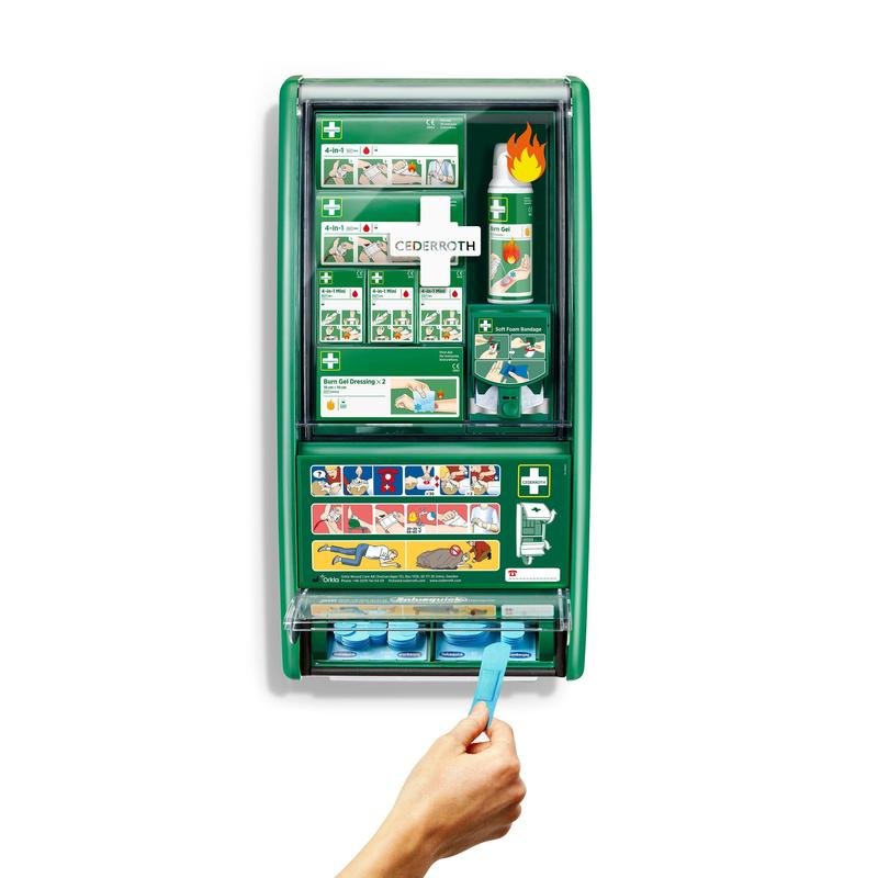 Une station de premiers secours & brûlures Cederroth verte d'Orkla Wound Care AB est montée sur un mur blanc, équipée de bandages, de gel pour brûlures, de rinçage oculaire et plus encore. Une main tire un bandage adhésif bleu du distributeur inférieur de la boîte de 1 unité.