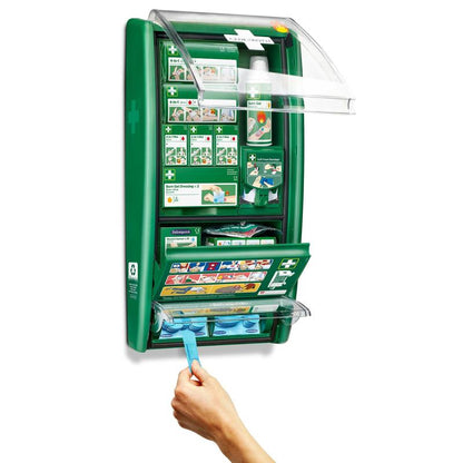 La station de premiers secours & brûlures Cederroth d'Orkla Wound Care AB est un ensemble vert monté au mur avec des compartiments étiquetés pour les bandages, les pansements et le gel pour brûlures. Une main tire un tissu bleu de l'unité ouverte révélant des fournitures organisées et des instructions claires.