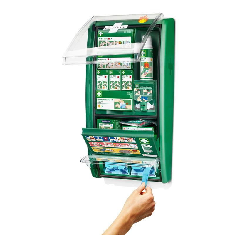 Une station de premiers secours & brûlures Cederroth d'Orkla Wound Care AB montée au mur est ouverte et montre des fournitures telles que des bandages, des instructions, des bouteilles de rinçage oculaire et une main qui prend une capsule de rinçage oculaire bleue du compartiment inférieur. (1 paquet/boîte).