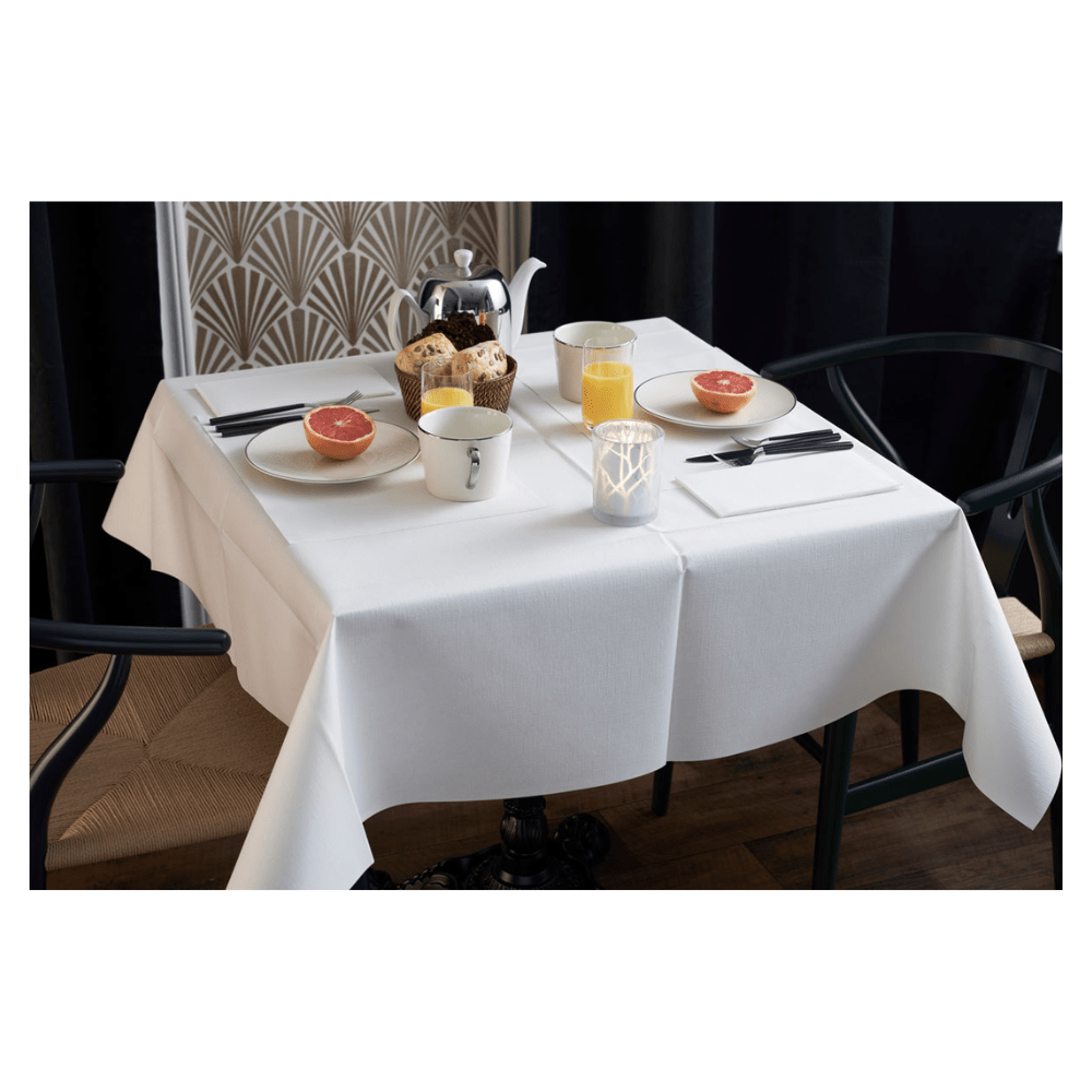 La table du petit-déjeuner est élégamment dressée avec une nappe blanche, deux chaises et un vase à motif géométrique. Sur la table se trouvent des moitiés de pamplemousse, des pâtisseries, du thé et du jus d'orange. Une serviette Duni Dunilin® (48x48 cm) de Duni GmbH ajoute du charme et de la fonctionnalité à l'ensemble matinal d'ambiance.