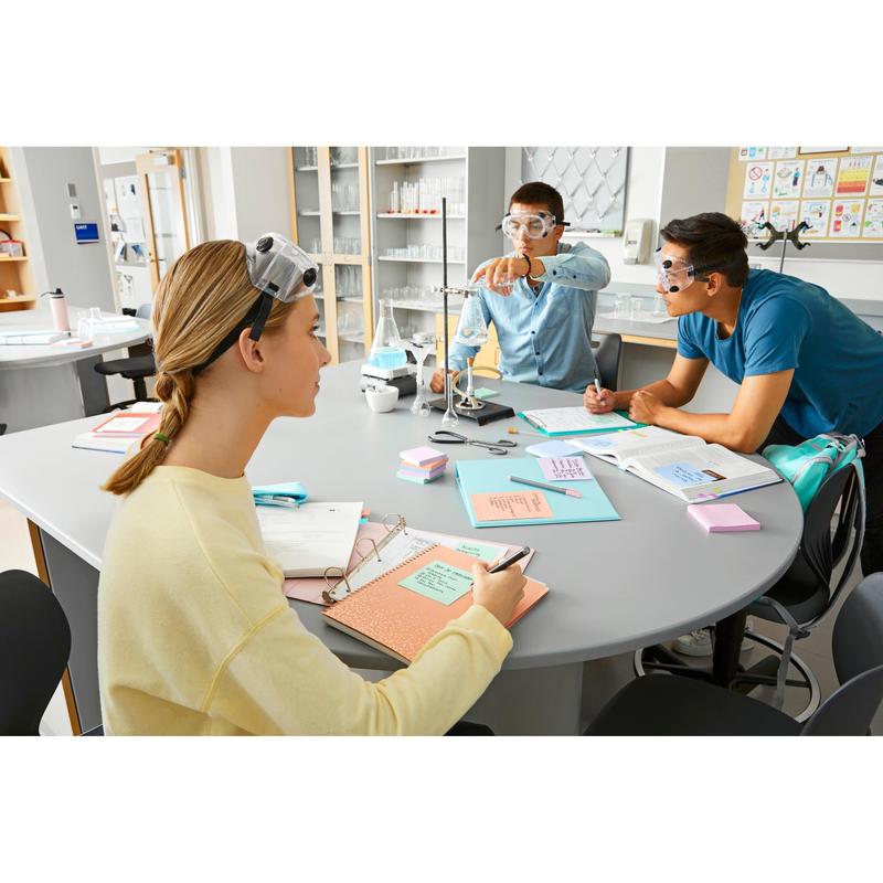 Trois étudiants avec des lunettes de protection sont assis à une table de laboratoire avec des manuels scolaires, des ustensiles de laboratoire et des Post-it® Super Sticky Notes (76 mm x 127 mm, 90 feuilles/bloc, 100% PEFC) de 3M Deutschland GmbH et prennent des notes, tandis que l'un ajuste une pince et les autres observent attentivement.