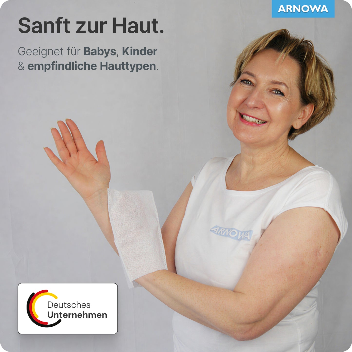 Une femme en chemise blanche sourit en tenant un gant de toilette jetable ARNOMED Spunlace avec PE, hydrofuge (sachet, 50 pièces) d'ARNOWA GmbH sur le bras. Le texte allemand souligne les soins doux pour les bébés, les enfants et les peaux sensibles.