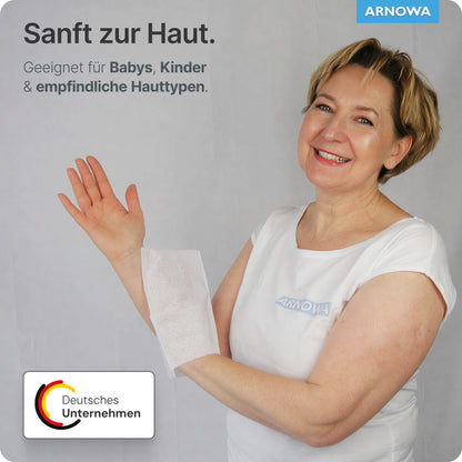Une femme en chemise blanche sourit en tenant un gant de toilette jetable ARNOMED Spunlace avec PE, hydrofuge (sachet, 50 pièces) d'ARNOWA GmbH sur le bras. Le texte allemand souligne les soins doux pour les bébés, les enfants et les peaux sensibles.